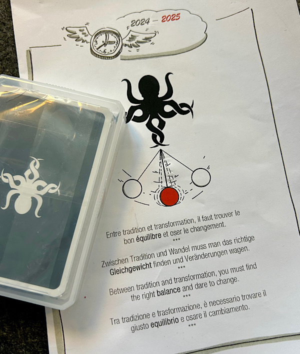 Ein Blatt mit einem Pendel und einem stilisierten Oktopus, daneben ein Stapel Spielkarten, ebenfalls mit dem Oktopus Signet