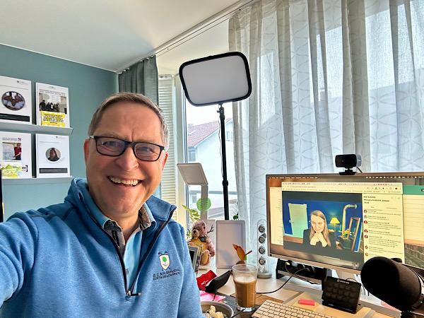 Mann mit Brille (Martin) vor dem PC mit Judith im Hintergrund